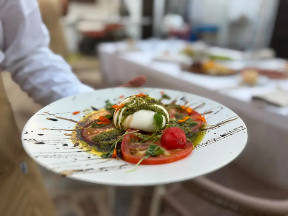 Burrata with heirloom tomato and pesto, plated and carried to table.